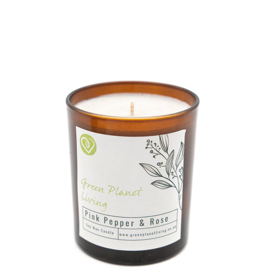 amber glass jar candle with biodegradable green planet living label with logo, pink pepper and rose and leaf sprig. photographed on a white background