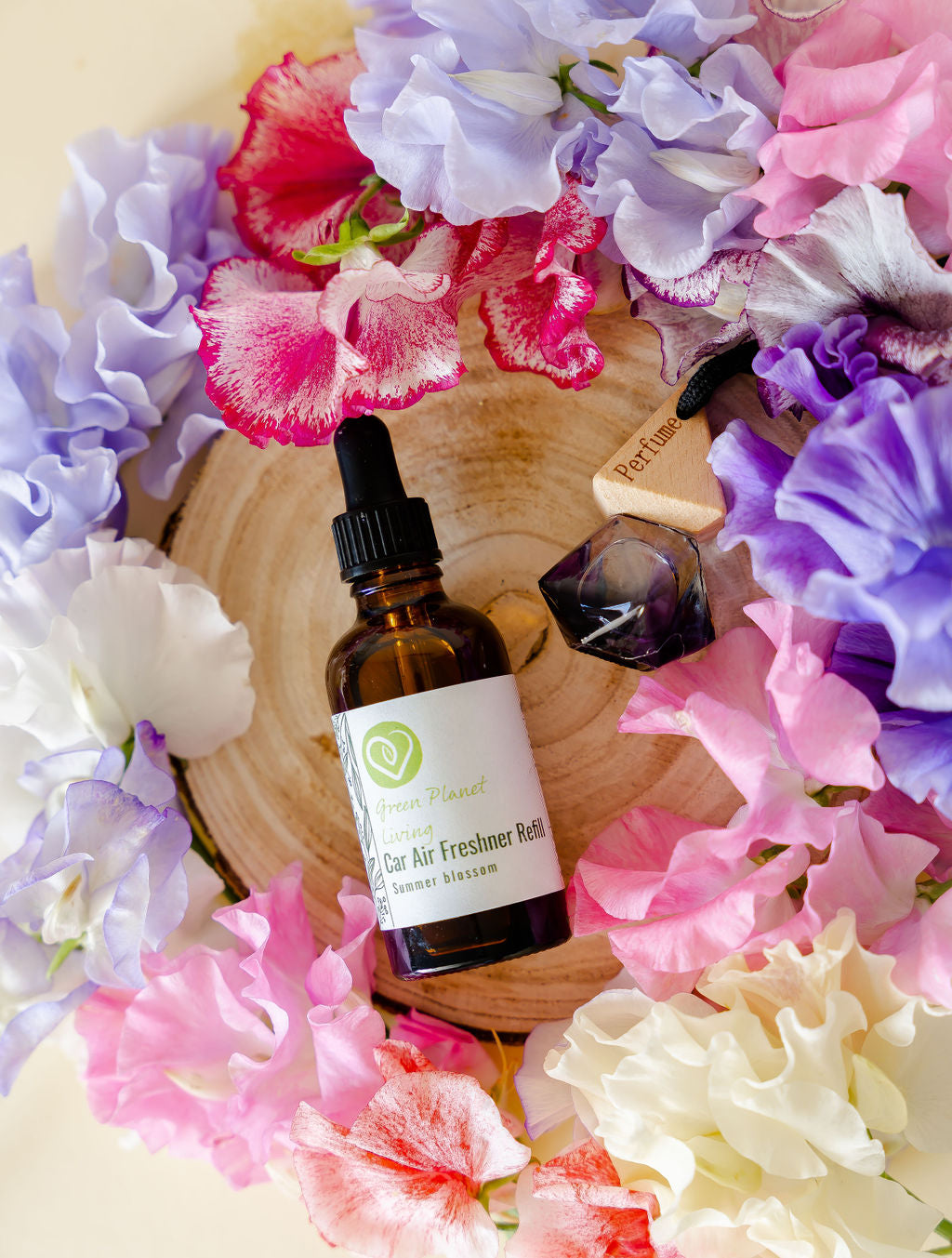Summer Blossom refill bottle and car diffuser placed on a round wood ring and surround in multi coloured sweet peas
