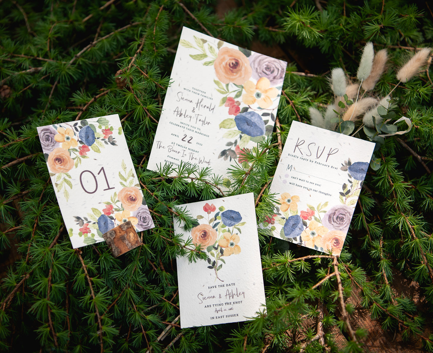 Seed paper wedding invite, rsvp, save the date and table numbers sat on a background of natural ferns.