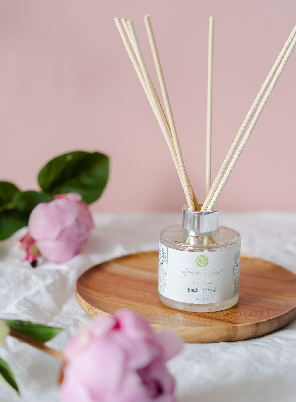 BLUSHING PEONY REED DIFFUSER WITH PINK BACGROUND ON A BAMBOO PLATE WITH LIGHT PINK PEONIES