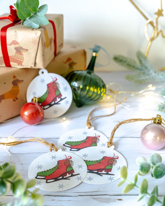 Festive plantable gift tags featuring red and green ice skates surrounded by snowflakes, displayed with Christmas ornaments and wrapped gifts.